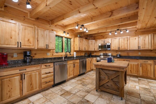 A wooden cabin-style kitchen with built-in cabinets, a central island, stainless steel appliances, and a window providing a view of greenery.