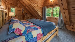 A cozy wooden cabin bedroom with a bed, a nightstand, a lamp, and a window with curtains. - Blue Ridge Lodge Hocking Hills: Accessible Luxury (Logan)