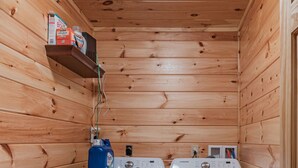 A laundry room with two washing machines, wooden walls, and a shelf with cleaning supplies. - Blue Ridge Lodge Hocking Hills: Accessible Luxury (Logan)
