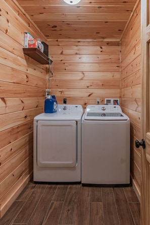 A laundry room with two washing machines, wooden walls, and a shelf with cleaning supplies. - Blue Ridge Lodge Hocking Hills: Accessible Luxury (Logan)