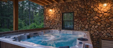 Un jacuzzi con un muro de piedra de fondo, vigas de madera y una ventana.