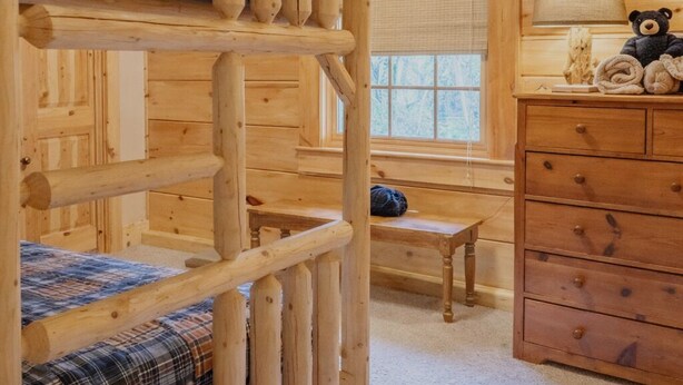 L’intérieur d’une cabane en bois, avec un lit superposé, une commode, une lampe et une fenêtre.