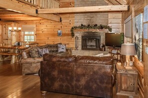 Ein Blockhaus-Interieur mit Kamin, Ledersofa, Esstisch aus Holz und einem Fernseher.