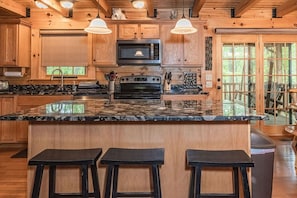 A kitchen with wooden cabinets, a granite countertop, a microwave, a stove, and three bar stools. - Black Bear Hideaway: Luxury Lodge in Hocking Hills (Rockbridge)