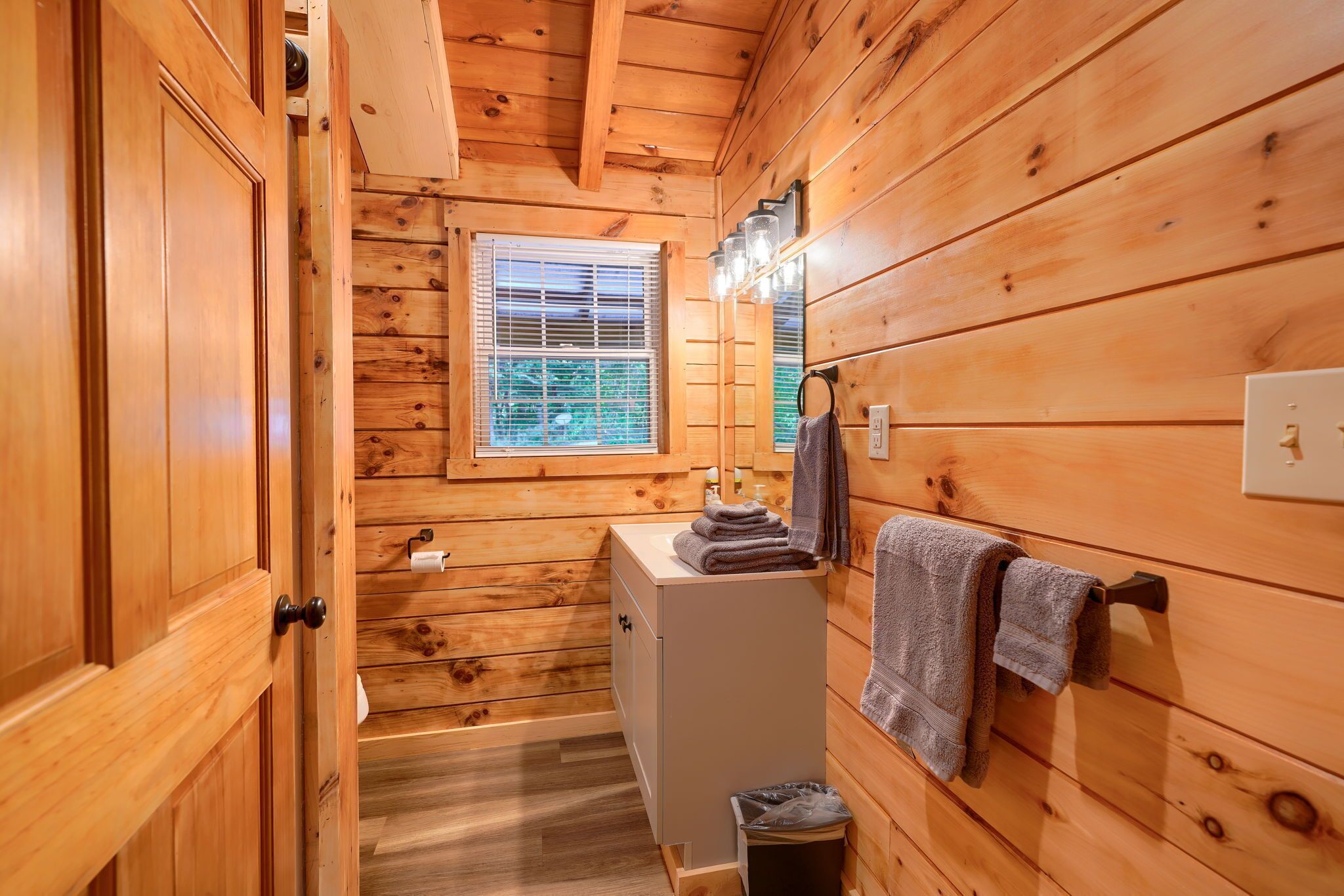 A wooden cabin bathroom with a window, a sink, and towels.