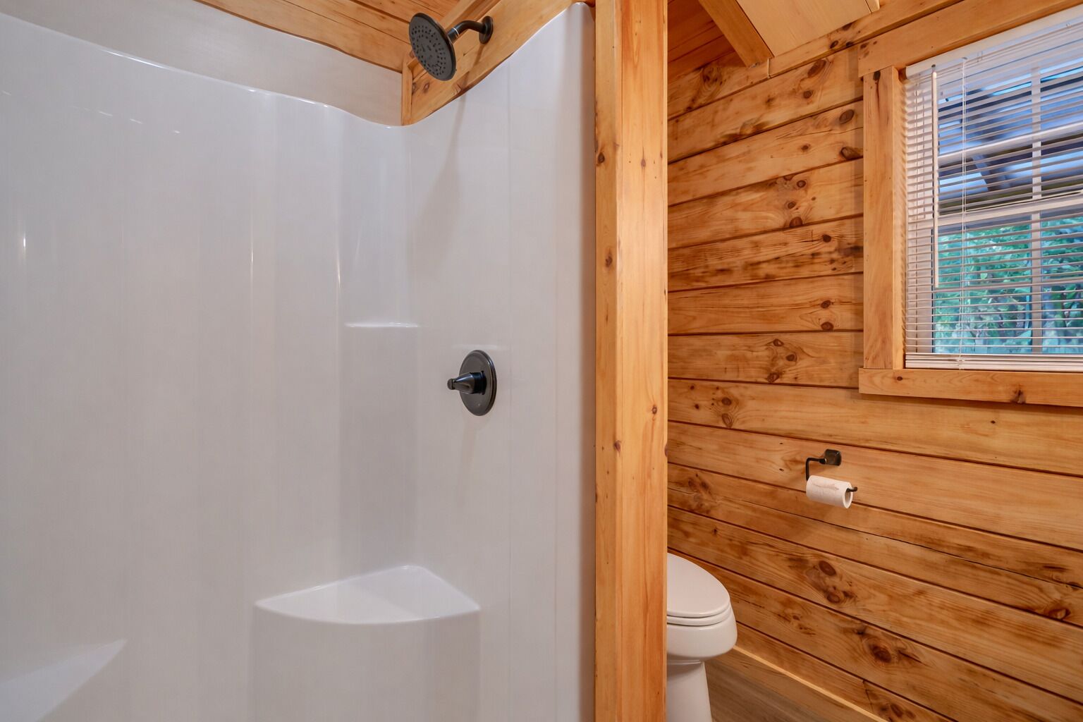 A wooden cabin bathroom with a shower, toilet, and window.
