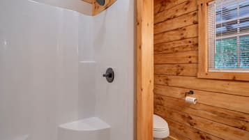 A wooden cabin bathroom with a shower, toilet, and window.