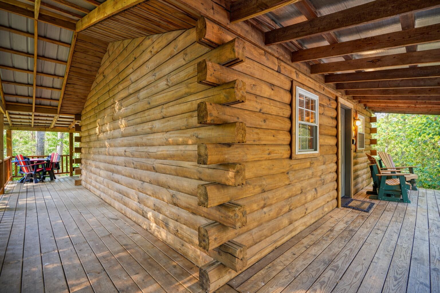 Una cabaña de troncos con un porche cubierto, una ventana y mobiliario exterior.