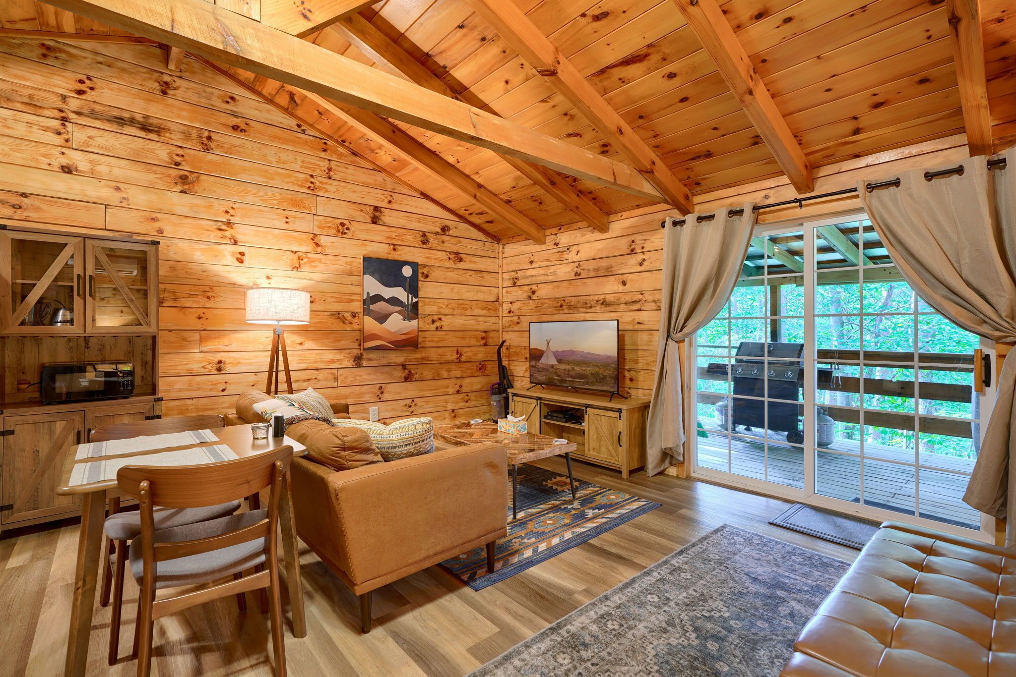A cozy cabin interior with a dining area, sofa, television, and a view of the outdoors.