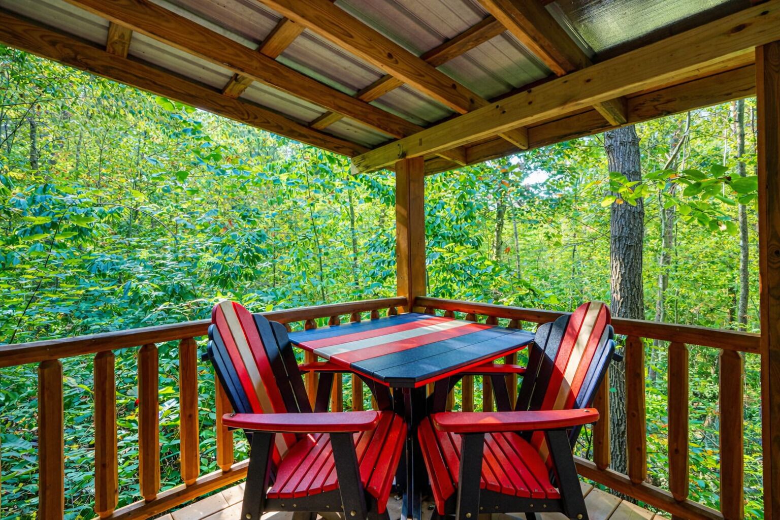 A wooden deck with a table and chairs, surrounded by a forested area.