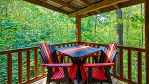 Eine Holzterrasse mit Tisch und Stühlen, umgeben von bewaldetem Gelände.