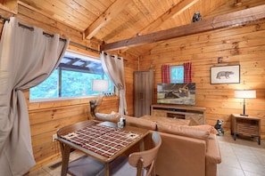 Ein gemütliches Blockhausschlafzimmer mit Holzbalkendecke, einem karierten Tisch, einer Couch, einem Fernseher und einer Bärenstatue.