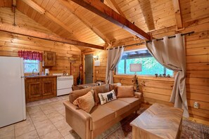 Interior acogedor de una cabaña con kitchenette, un sofá y una ventana con cortinas.