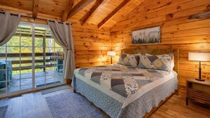 A wooden cabin bedroom with a large bed, two bedside lamps, and a window with curtains.
