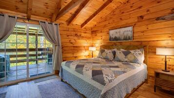 A wooden cabin bedroom with a large bed, two bedside lamps, and a window with curtains.