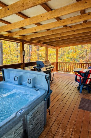 Una terraza de madera con jacuzzi, parrilla y sillas tipo Adirondack.