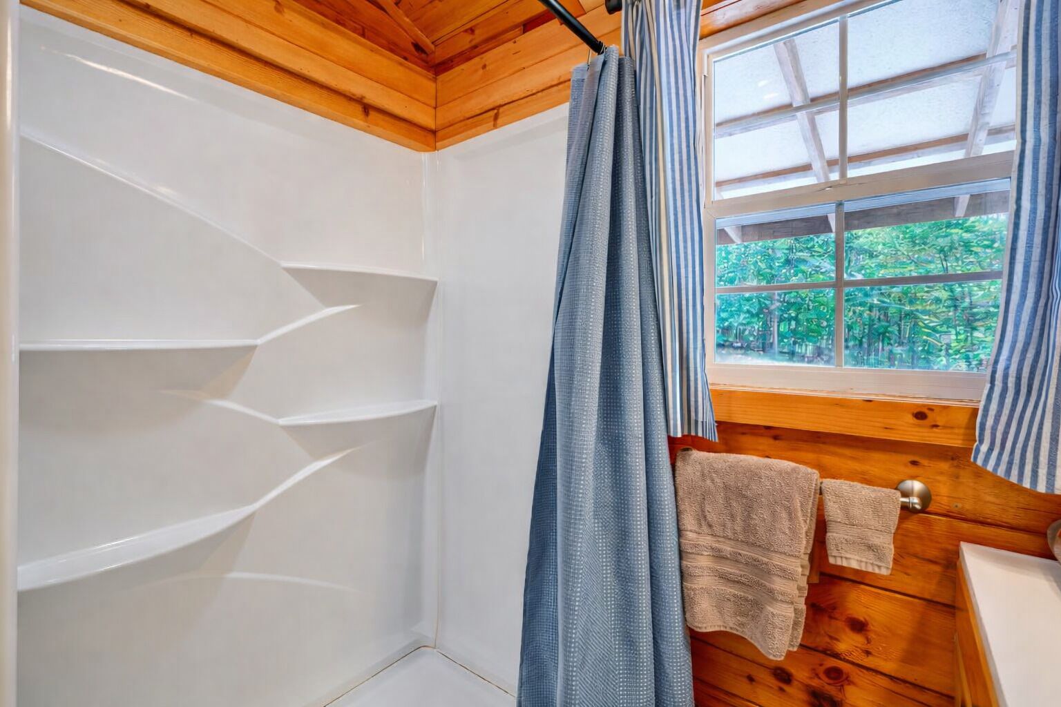 Un baño con techo de madera, una ventana con vista a follaje y un perchero con una toalla.
