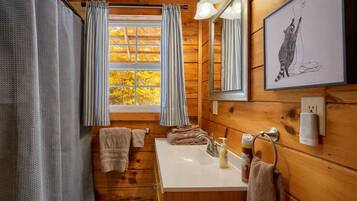 Ein Badezimmer einer Holzhütte mit Fenster, Waschbecken und Spiegel.