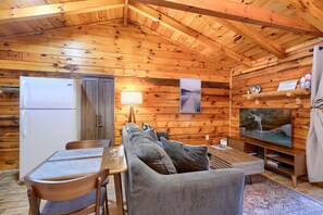 Un acogedor interior de cabaña con techo de madera, una zona de comedor con mesa y sillas, un sofá, un televisor y un refrigerador.