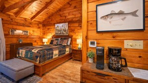 Une chambre confortable, aménagée dans le style d’un chalet, avec un lit, une petite table et une machine à café, ainsi qu’une illustration encadrée représentant un poisson, accrochée au mur.