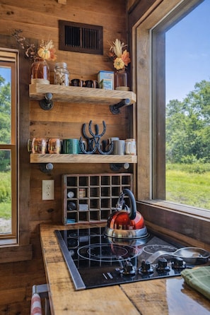 A kitchen with a built-in stove, wooden shelves, and a window with a view of greenery.