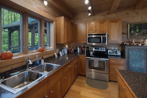 A modern kitchen with wooden cabinets, stainless steel appliances, and a large window overlooking a wooded area. - Pumpkin Ridge Resort: 2 spaces for one rate (New Plymouth)