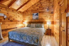 Een slaapkamer in een houten chalet met een bed, twee bedlampjes, een nachtkastje en een lijst met een foto aan de muur.
