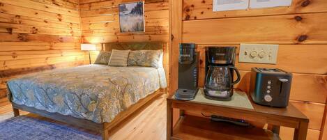 Ein Zimmer in einer Holzhütte mit einem Bett, einer Kaffeemaschine, einem Toaster und einer Uhr an der Wand.