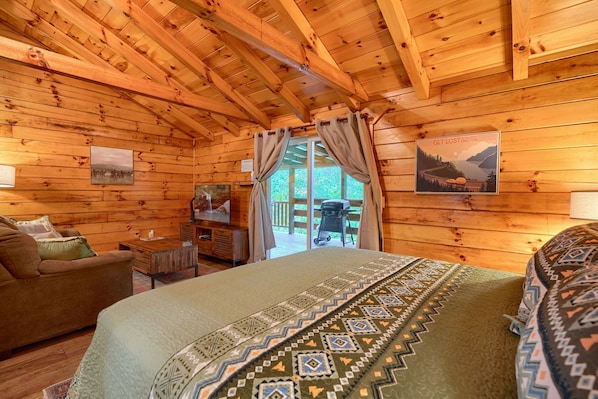A cozy log cabin room with a bed, a television, and a view of the outdoors.