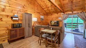 A cozy cabin interior with a wooden ceiling, a sofa, a dining table, and a television.