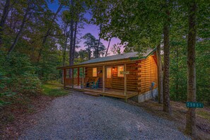 A rustic cabin with a porch, a small deck, and a gravel driveway.