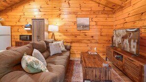 A cozy log cabin interior with a sofa, television, wooden cabinet, and a kitchen area.