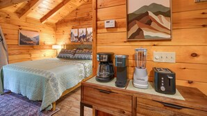 A cozy wooden cabin room with a bed, a coffee maker, a blender, and a toaster on a wooden table.
