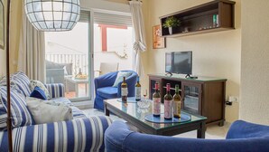 En stue med sofa, sofabord med vinflasker, fjernsyn og balkon med udsigt.