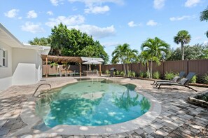 A backyard with a swimming pool, patio furniture, and a pergola.