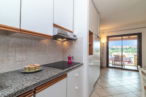 A kitchen with a black countertop, a pink electric kettle, and a window leading to a balcony with a table and chairs.