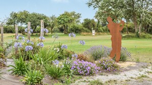 En skulptur af en person i et mark med forskellige blomster og træer i baggrunden.