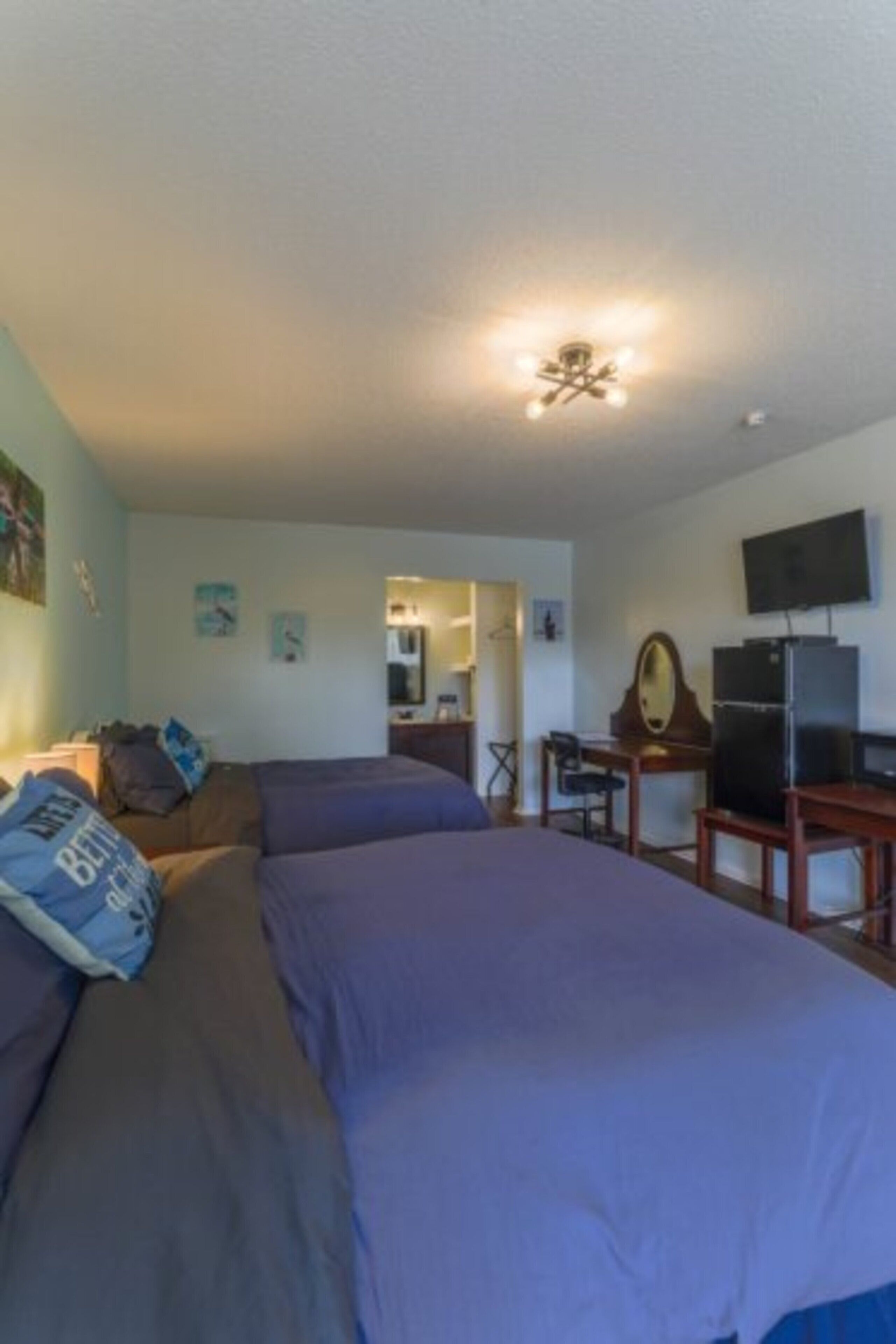 A bedroom with a bed, a desk, a chair, a television, and a ceiling light fixture.