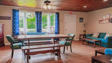 A room with a wooden ceiling, a table with benches, a sofa, and a view of greenery outside.