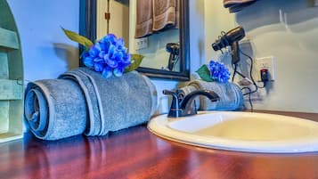 Un bagno con un mobile bagno in legno, un lavandino e un porta asciugamani con asciugamani arrotolati e un fiore blu decorativo.