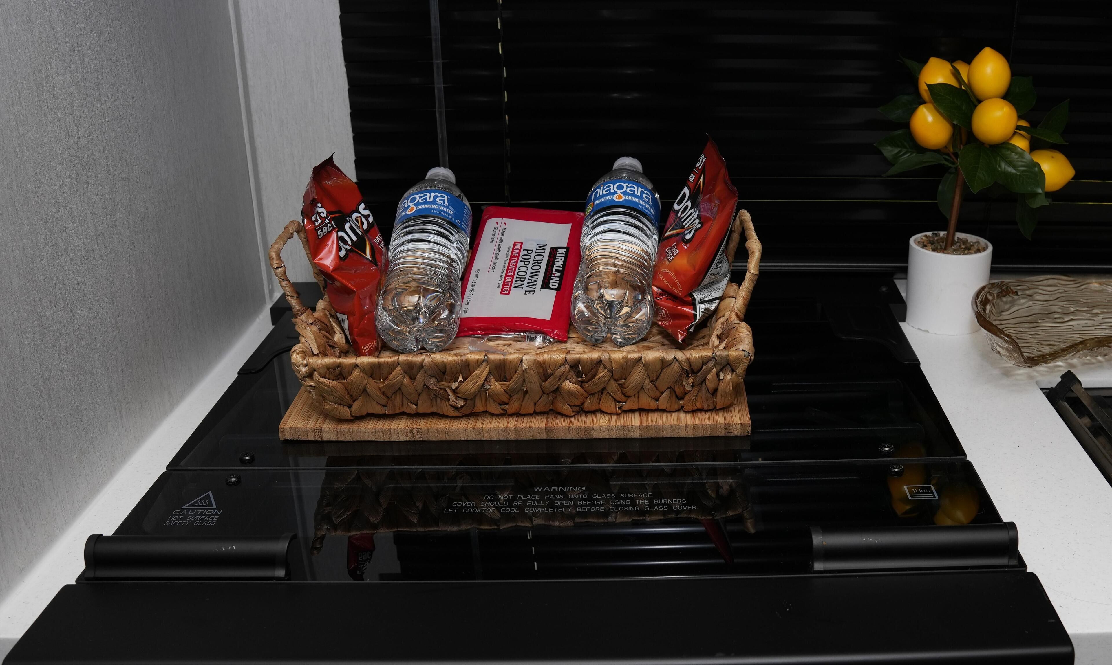 A kitchen with a microwave, a glass safety surface, and a basket containing food items.