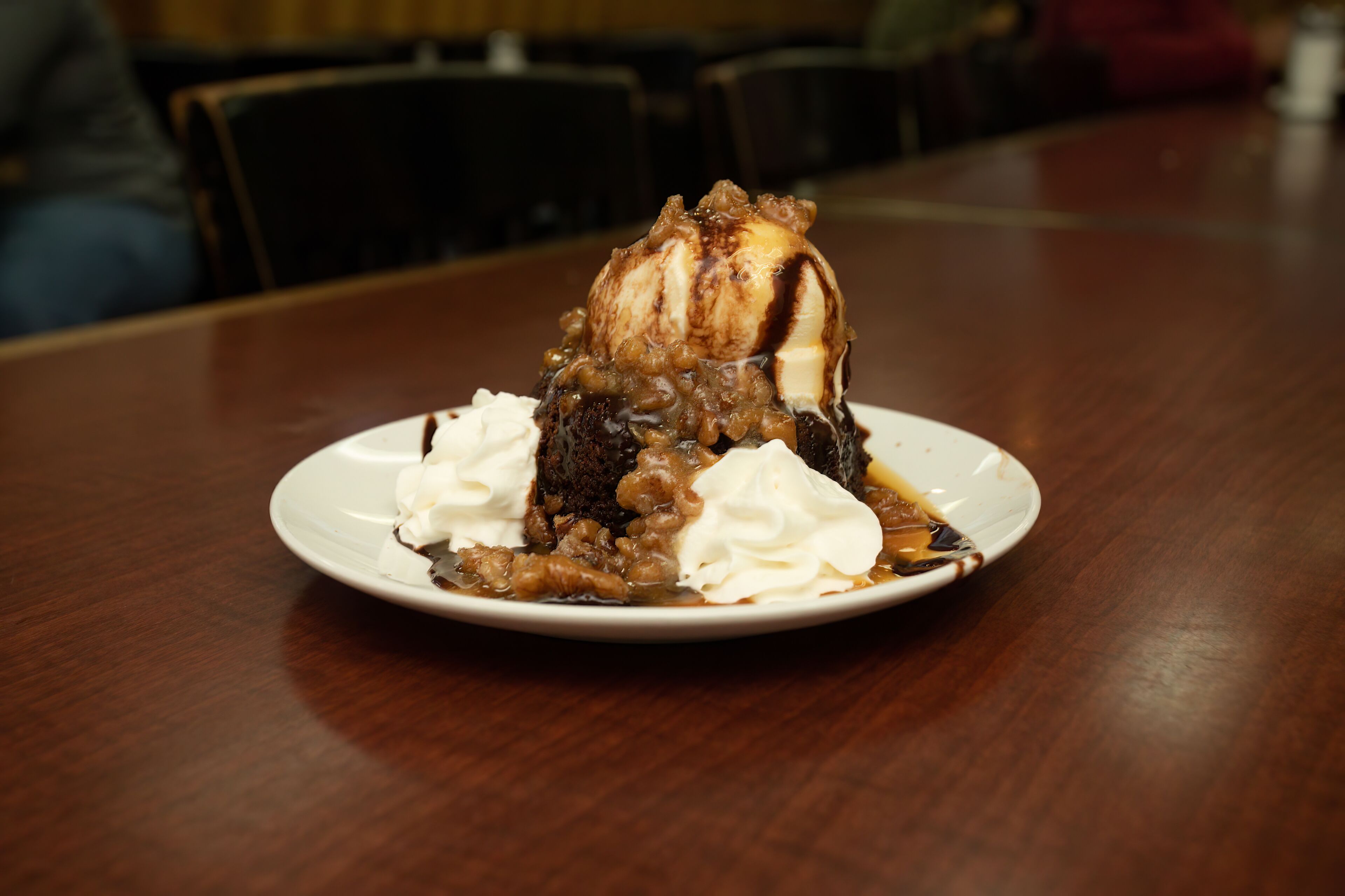 Dessert auf einem weißen Teller mit Karamellsauce und Schlagsahne auf einer Holztischplatte.