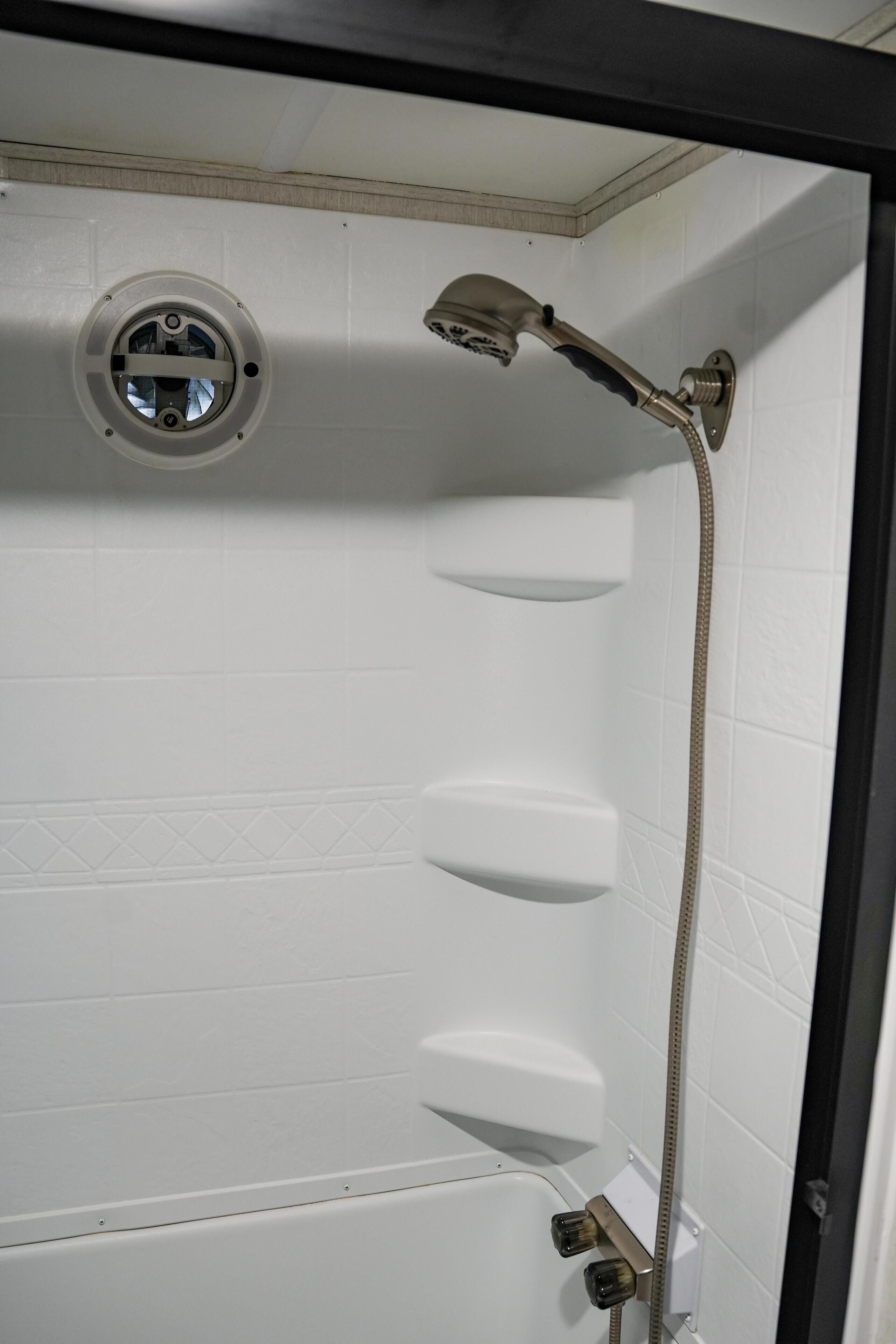 A shower with a handheld showerhead and a wall-mounted control panel.