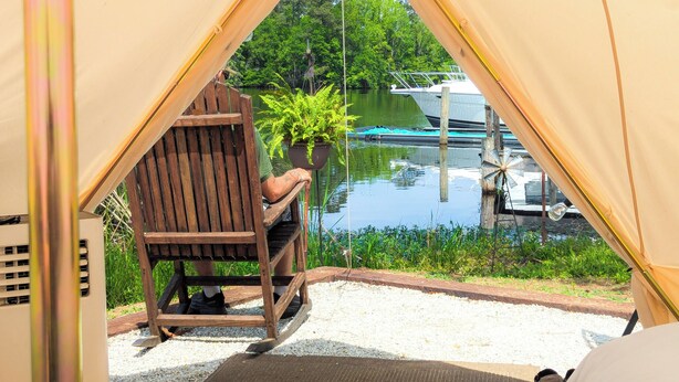 Une tente avec vue sur un lac et des bateaux, une chaise en bois et une plante en pot.