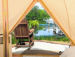 Ein Zelt mit Blick auf einen See und Boote, ein Holzstuhl und ein Blumentopf.