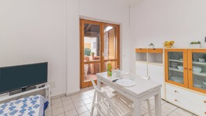 A compact kitchen with a dining area, a TV on a stand, and a small table with chairs. - Piazzetta Bilo Brezza Marina (Loiri Porto San Paolo)