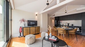 A modern living room with a dining area, a kitchen, and a television on a cabinet.