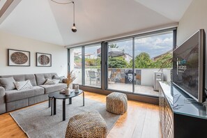 A modern living room with a grey sofa, a coffee table, and a TV. Large windows offer a view of the outside. - Modern loft in the heart of Porto (Porto)