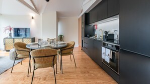 A modern kitchen with dark cabinetry, a built-in oven, and a dining area with wicker chairs and a round table.