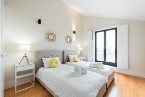 A modern bedroom with two beds, a bedside table with a lamp, decorative wall mirrors, and a large window with a view. - Modern loft in the heart of Porto (Porto)